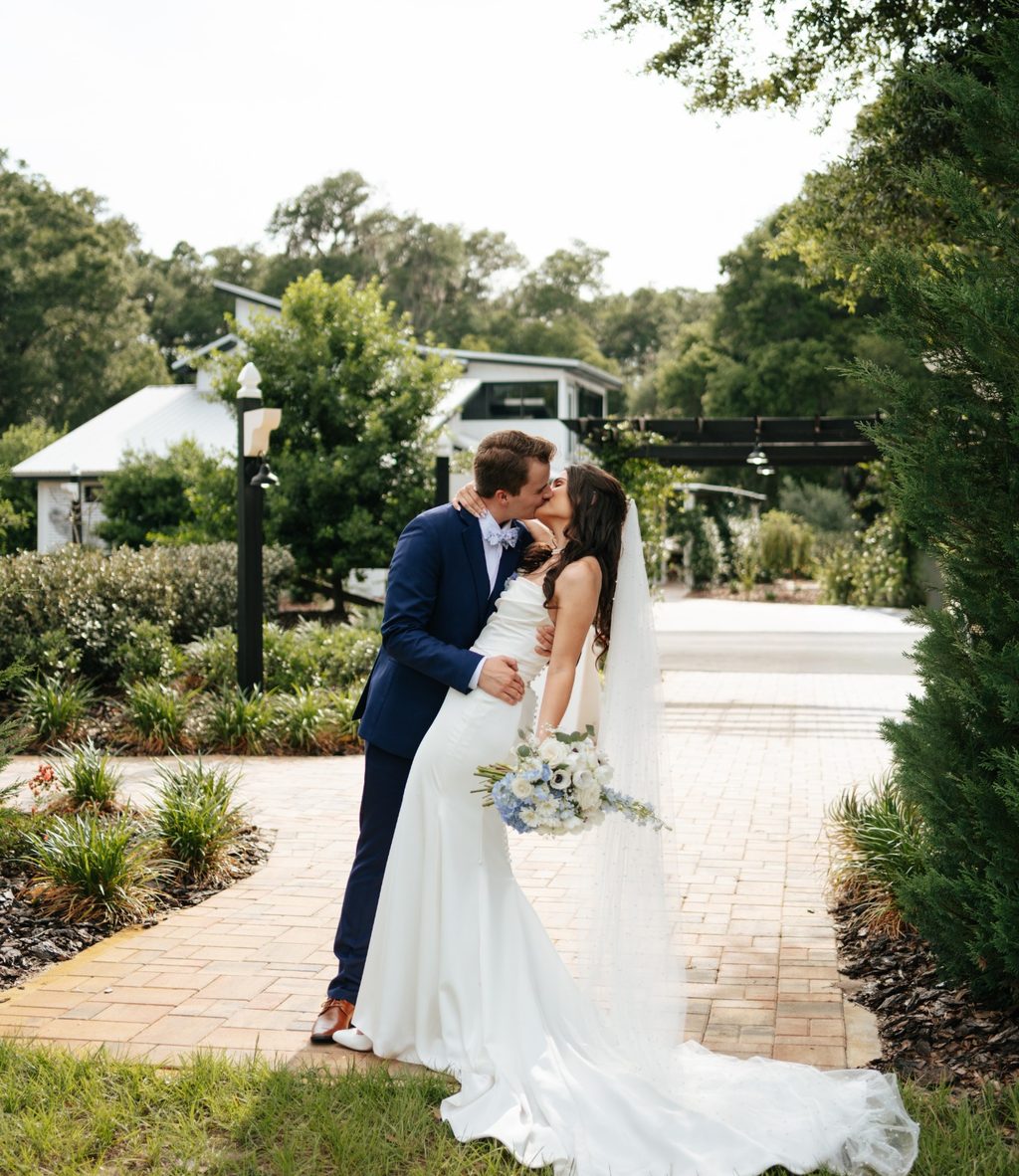 Bride and groom sharing a kiss at Villa Serafina during their wedding day, surrounded by lush landscaping and the venue's garden walkway.